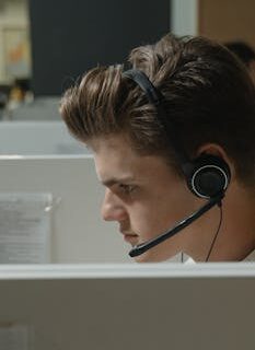 Close-up of a focused male call center agent wearing a black headset at work.