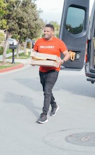 Delivery man in red shirt carrying package from van on a sunny street.